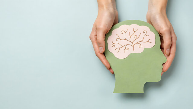 Hands holding a green paper cutout of a human head silhouette with a brain