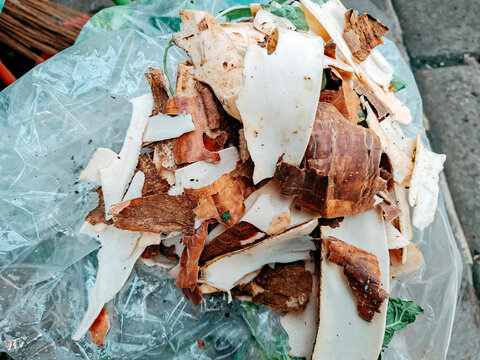 A collection of dry brown cassava skin peels and vegetable waste gathered inside a clear plastic bag.