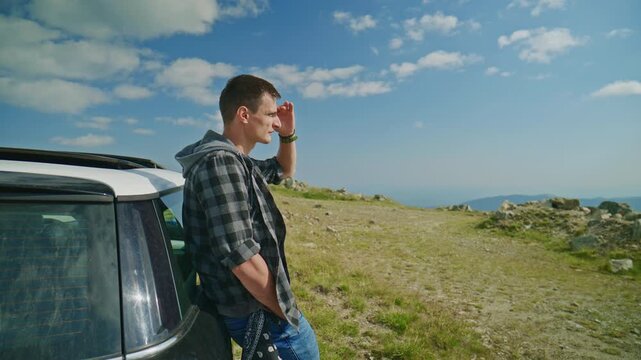 Person stands next to a car looking at the horizon from a hill on a clear day with blue sky and scattered clouds