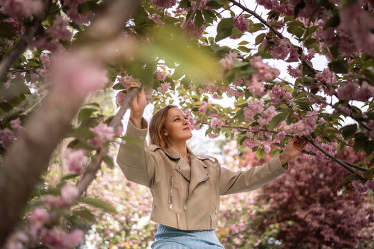 Blooming cherry trees frame a serene woman in a stylish leather jacket during a vibrant outdoor seasonal spring walk
