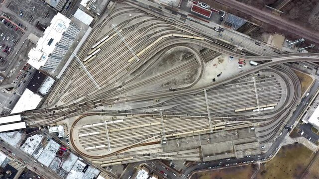 Vertical aerial perspective looking directly down over an extensive rail yard with curving tracks, railway switches and trains forming intricate patterns within an urban environment.