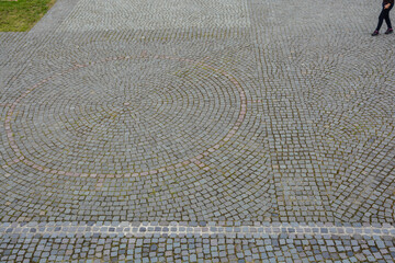 Fototapeta premium Abstract cobblestone pattern with a circular design and partial view of a person walking.