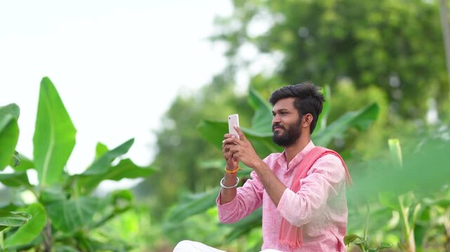 Young indian farmer sitting at banana agriculture field and using mobile phone 
