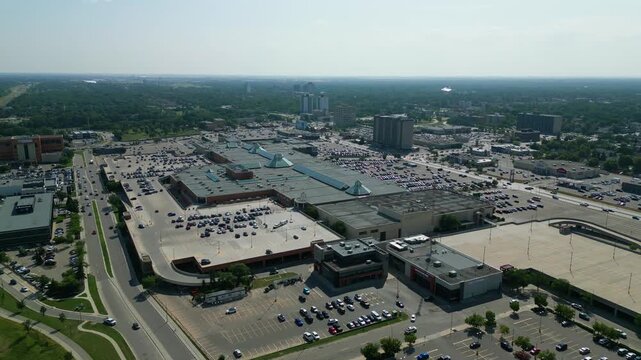 Aerial drone shot flying backward from CF Polo Park to reveal the larger shopping district, parking areas, roadways, and surrounding Winnipeg cityscape