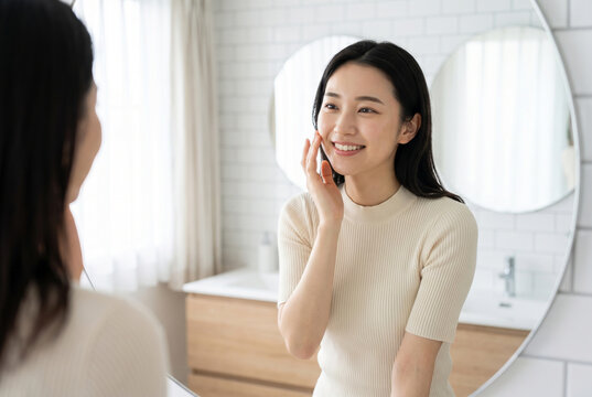 洗面台の鏡を見て微笑むスキンケア中の女性 Generative AI