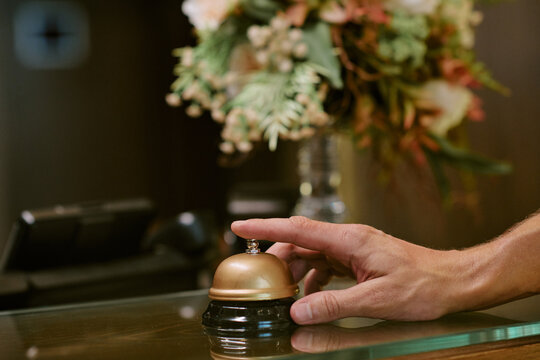 Hand of unrecognizable man ringing service bell on reception desk in hotel lobby, calling for assistance. Close up shot representing hospitality industry and customer service concepts