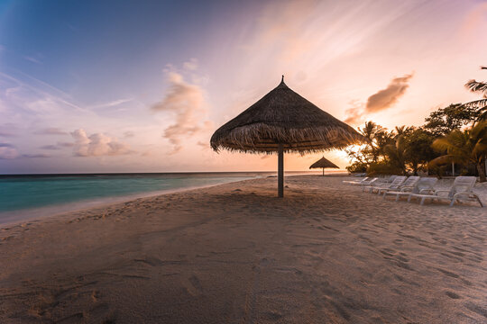 Tropical Maldives beach with thatched parasol at sunset