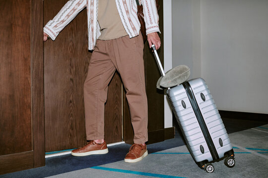 Cropped shot of unrecognizable man pulling suitcase and opening hotel room door. Image represents business travel and hospitality services, ideal for tourism marketing
