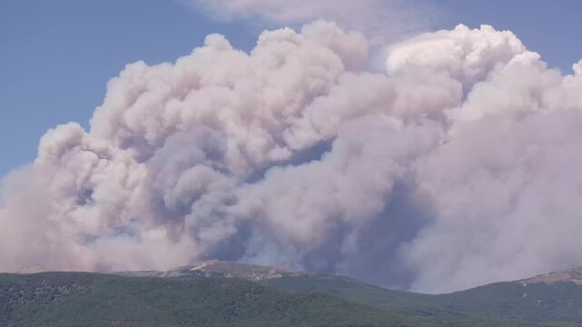 Telephoto drone footage at 167mm with a lateral pan across the Central Mountain Range, showing unburned forests in the foreground beneath an immense pyrocumulus cloud above the Ti&eacute;tar Valley.