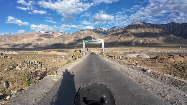 Padum, India : Point of view footage of motorcycle rider enters gate to Padum, high-altitude mountain road in Ladakh of India with prayer flags on the roadside on sunny late afternoon with shadow
