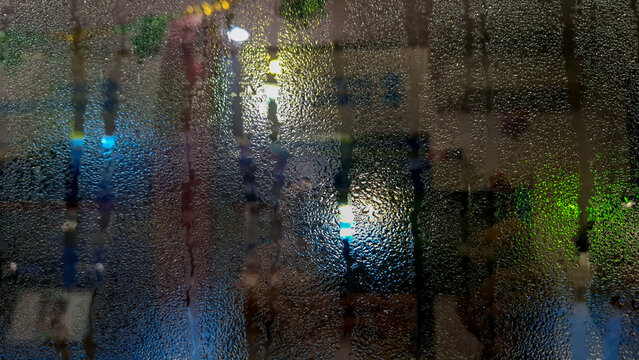 Detailed view of heavy water condensation droplets on a glass window reflecting colorful indoor lighting and bokeh blur at night.