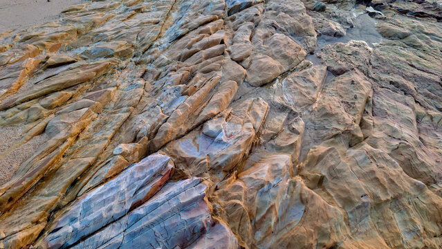 High-angle perspective of rugged brown rock formations and tidal pools along the beach coast exposed during low tide.