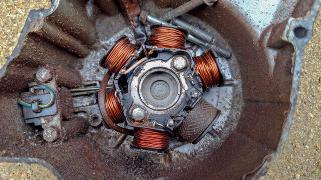 Close-up of an old motorcycle engine stator coil with copper wire windings inside a rusty metal casing. Perfect for mechanical, automotive, and repair concepts.