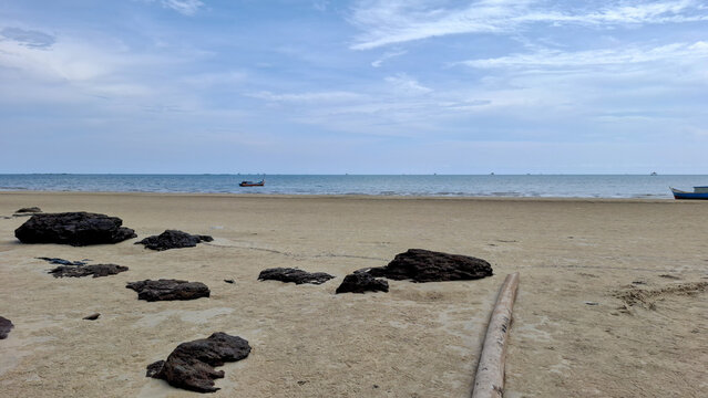 Minimalist view of small dark rock outcroppings along a vast sandy shore stretching to a calm horizon with small boats in the far distance.