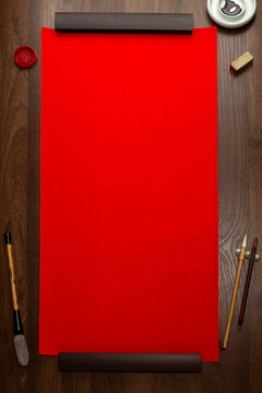 Blank red Chinese calligraphy rice paper scroll mockup on dark wooden background with ink brushes and seals top view