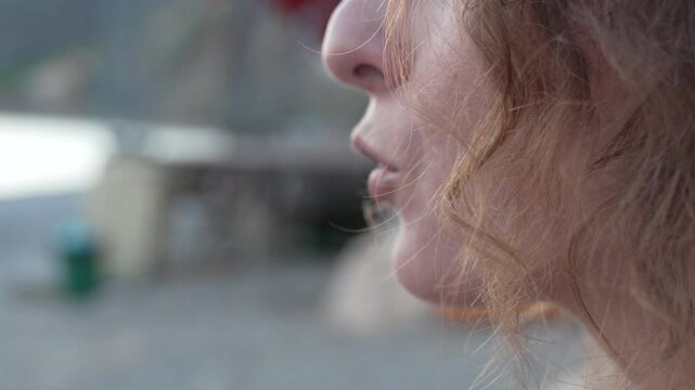 Eating snack outdoors by the ocean. Close up profile shot of curly hair woman.