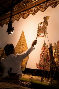 Indonesian dalang puppeteer performing wayang kulit shadow puppet show behind lit screen