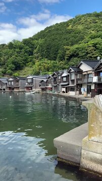 Traditional Japanese boat houses Funaya in Ine town along coastal bay water with lush green mountain background in Kyoto Japan