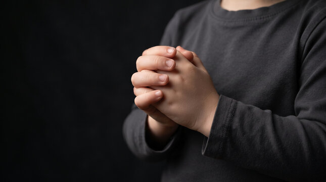 Child's hands clasped together in prayer or contemplation against a dark background