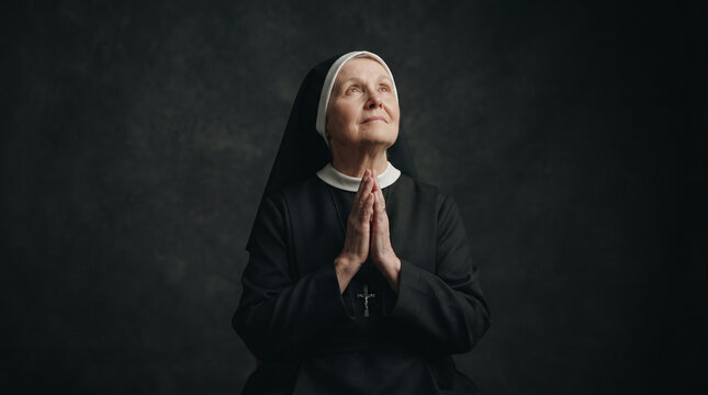 Elderly nun praying with hands clasped and looking upwards in quiet devotion