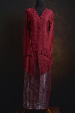 Maroon embroidered kebaya with songket skirt and shawl displayed on a dress form