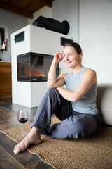 Fototapeta premium Young woman spending quiet evening by fireplace, relaxing with drink in modern cozy home, lifestyle and comfort concept