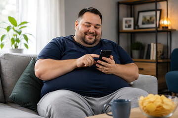 Fototapeta premium Overweight man sitting in armchair using smartphone at home