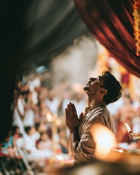 Bengali man praying with palms together at a glowing pandal during aarti, featuring warm amber light and incense haze for festive sweets and FMCG brands
