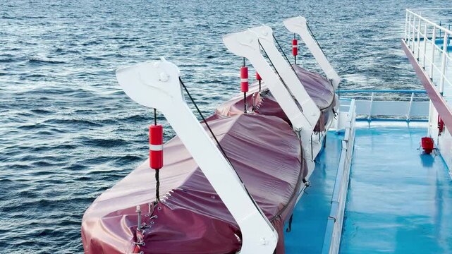 Covered lifeboats rest on a cruise ship deck as it sails across Lake Ladoga. The calm water flows below under daylight. This secure view brings a feeling of safety and peace.