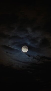 bright full moon partially covered by moving dark clouds at night, creating a mysterious and dramat