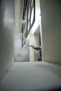 Worker spraying industrial metal panel in paint booth with mist and bright lighting