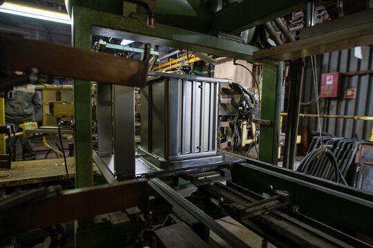 Metal appliance casing on factory assembly line with industrial machinery and worker in background
