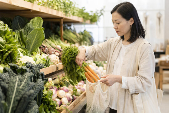 Korean shopper placing loose vegetables in a reusable mesh bag