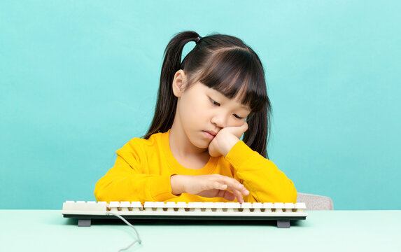 Bored Asian school girl resting head while using keyboard isolated on blue background, tired emotion, screen fatigue and education concept