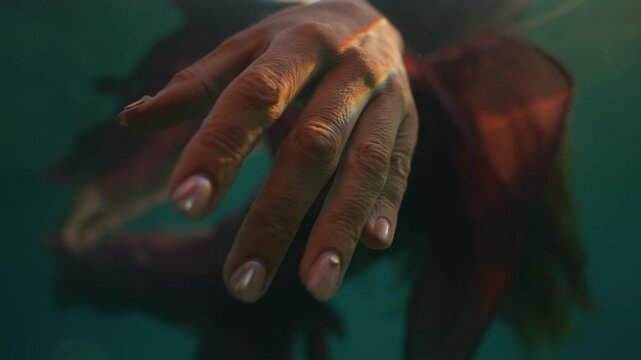 Underwater close up of a leg wearing an anklet, dress fabric drifting alongside.