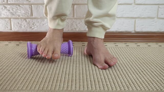 Person massaging feet using spiky roller for plantar fasciitis. Barefoot man rolling his foot over a purple massage roller for acupressure therapy at home, relieving arch pain