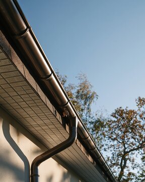 Modern house gutter and downpipe with textured shingled roof and beige cladding, showing seasonal autumn leaves for home maintenance and roofing services