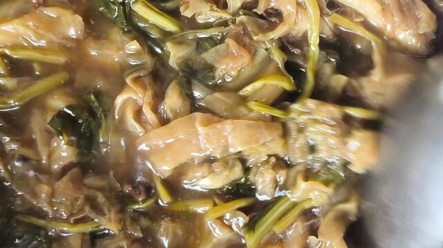 Close-up of traditional Thai-Chinese vegetable stew (Tom Jab Chai) being stirred with a ladle in a hot wok.