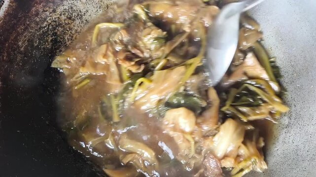 Close-up of traditional Thai-Chinese vegetable stew (Tom Jab Chai) being stirred with a ladle in a hot wok.