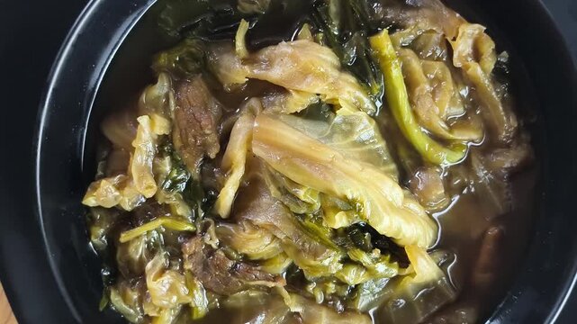 A top-down rotating shot of traditional Thai-Chinese mixed vegetable stew (Tom Jab Chai) served in a black bowl.