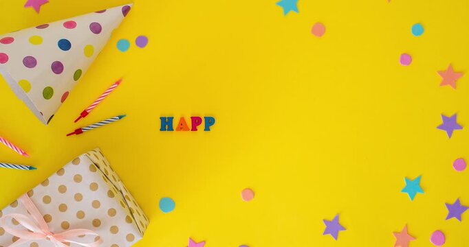 Birthday flat lay with a party hat, festive candles, a gift and an inscription Happy Birthday on a yellow background. Stop motion animation