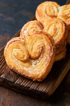 Cookies in the shape of rustic wooden platters, French palmier cookies, adorned with a sweet heart-shaped puff pastry encased in a sugary coating. Golden-baked desserts, with a dark backdrop, homemade