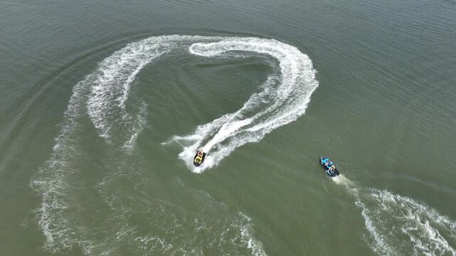 Aerial view of personal watercraft making high speed turns and white foam trails on river surface.