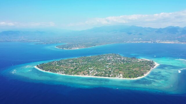 Stunning aerial motion of idyllic tropical island with white sand beaches and vibrant turquoise water, surrounded by deep blue ocean with distant mountains.