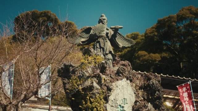 An imposing winged tengu statue, a mythical guardian spirit deeply associated with Hansobo Shrine, rises above the treeline against a clear blue sky in Kamakura, Japan.