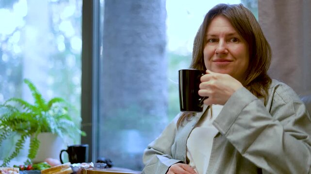 A mindful woman sips warm coffee while relaxing in a cozy interior. This peaceful lady pauses to enjoy a serene morning ritual. A calm adult finds tranquility in a quiet corner.