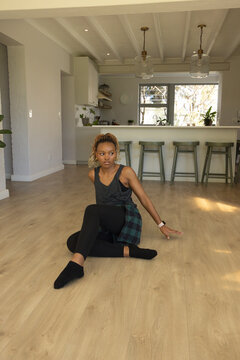African American woman sitting on wood floor in open-plan kitchen, wearing smartwatch