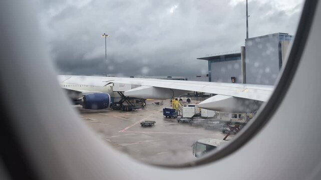 Looking out the airplane window on a rainy day, airport terminal preparing for departure