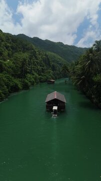 Vertical drone follows a Loboc River cruise boat downstream through green water between forested hills in Bohol