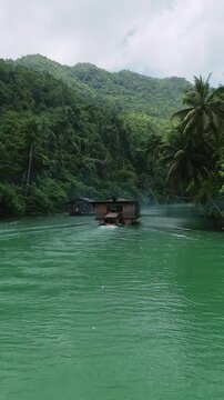 Vertical drone ascends while following Loboc River cruise boats downstream through green water and forested hills in Bohol